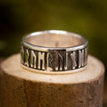 Bild in Galerie-Betrachter laden, Sølvring Uovervindelig 925s Sølv, en sølvring med indviklede futhark-runer, hviler på en tekstureret træoverflade, sat mod en sløret grøn baggrund. Ringens indgraveringer, lavet af ægte sølv, består af ældgammelt udseende symboler, der omslutter hele båndet.