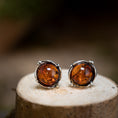 Bild in Galerie-Betrachter laden, Ein Paar Ohrschmuck Amber Key 925s Silber ruht auf einer Holzoberfläche. Die satten, warmen orangebraunen Steine sind in einer detailreichen Silberfassung mit kleinen Zierperlen eingefasst, perfekt vor dem unscharfen Hintergrund.