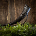 Bild in Galerie-Betrachter laden, En elegant Drikkehorn Basic uden holder med en mørk nuance vises elegant på et sort metalstativ, sat mod en træbaggrund. I forgrunden introducerer sløret grønt løv et strejf af naturlig kontrast til den rustikke scene, hvilket fremkalder atmosfæren af traditionel vikingemarkeder.