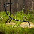 Bild in Galerie-Betrachter laden, Et rustikt sort metal- og træflaskestativ formet som en cykel, placeret på grønt græs med en træhegnbaggrund. Stativet, der minder om vikingemarkeder, har en cirkulær træbund til hjulene, hvilket giver den et vintage-udseende. Drikkehorn Rune ville føle sig hjemme her.
