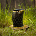 Bild in Galerie-Betrachter laden, Et poleret Drikkeglas Horn med Mønster (100ml) med guldkant og indviklede udskårne mønstre er placeret på en træbund, omgivet af grønt græs. Baggrunden viser et rustikt plankeværk.