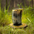 Bild in Galerie-Betrachter laden, Et Drikkeglas Horn med Mønster (100ml) med en gylden kant sidder oprejst på en cirkulær træbund i græs. Hornet, der har et diamantmønster og en blank finish, er sat mod en baggrund af sløret grønt og træplanker, hvilket fremhæver dets unikke håndværk.