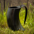 Bild in Galerie-Betrachter laden, Et Vikingekrus Nature Horn (600-800ml) med et sort, hornformet design og et buet håndtag sidder på grønt græs, sat mod en sløret træbaggrund. Dette krus efterligner et traditionelt drikkehorn, perfekt til dem, der værdsætter historien og æstetikken ved store drikkekrus.