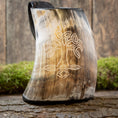 Bild in Galerie-Betrachter laden, Vikingekrus Yggdrasil Horn, et drikkekar med træhorn med et udskåret Yggdrasil trædesign, vises opretstående på en stenoverflade. Mos og en forvitret træbaggrund fremhæver de rustikke omgivelser. Denne 600-800 ml, vikinge-inspirerede krus fremviser naturlige, jordnære nuancer og indviklet håndværk.