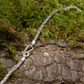 Bild in Galerie-Betrachter laden, Et nærbillede af Halskæden ByKila Drageben 3mm 925s Sølv-kædearmbånd med et indviklet design og krogspænde, lagt på en struktureret træbark med grønt mos omkring sig.