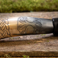 Bild in Galerie-Betrachter laden, Nærbillede af Drikkehorn Yggdrasil med Mønster, der viser dens polerede overflade prydet med indviklede udskæringer. Designet har et sammenflettet knudemønster til venstre, der går over til et træmotiv med detaljerede blade i midten og til højre. Hornet hviler på en rustik træholder, der minder om vikingemarkeder.