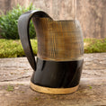 Bild in Galerie-Betrachter laden, Et håndlavet Vikingekrus Bark Horn (600-800ml) med en poleret mørkebrun top og en lysebrun bund sidder på en rustik træoverflade med grønt i baggrunden. Denne ølkrus har et glat, buet håndtag og lodrette riller langs den øverste halvdel for tekstur.