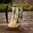 Bild in Galerie-Betrachter laden, En Mini Vikingekrus Horn Wave (100 ml) med indviklede keltiske knudeudskæringer og et glat håndtag sidder på en rustik træoverflade. Hornkrusen fremviser en blanding af sorte, hvide og beige nuancer, og dens flade base gør, at den kan stå oprejst.