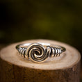 Bild in Galerie-Betrachter laden, Sølvring Spiral 925s Sølv er elegant placeret på en træoverflade. Denne sølvring kan prale af et slående spiraldesign i midten, med indviklet wirework, der fremhæver spiralen, der afspejler vikingernes håndværk. Baggrunden er blødt sløret med jordnære og grønne nuancer.
