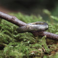 Bild in Galerie-Betrachter laden, En rustik, naturinspireret ring på en mosbevokset overflade. Ringen, kendt som Fingerring - Eryn Design - Branches, har en trætekstur og en lille indlejret diamant, der fremkalder en naturlig, jordagtig æstetik. Den fremviser dansk design, den sidder fint på en kvist og blander sig problemfrit med omgivelserne.
