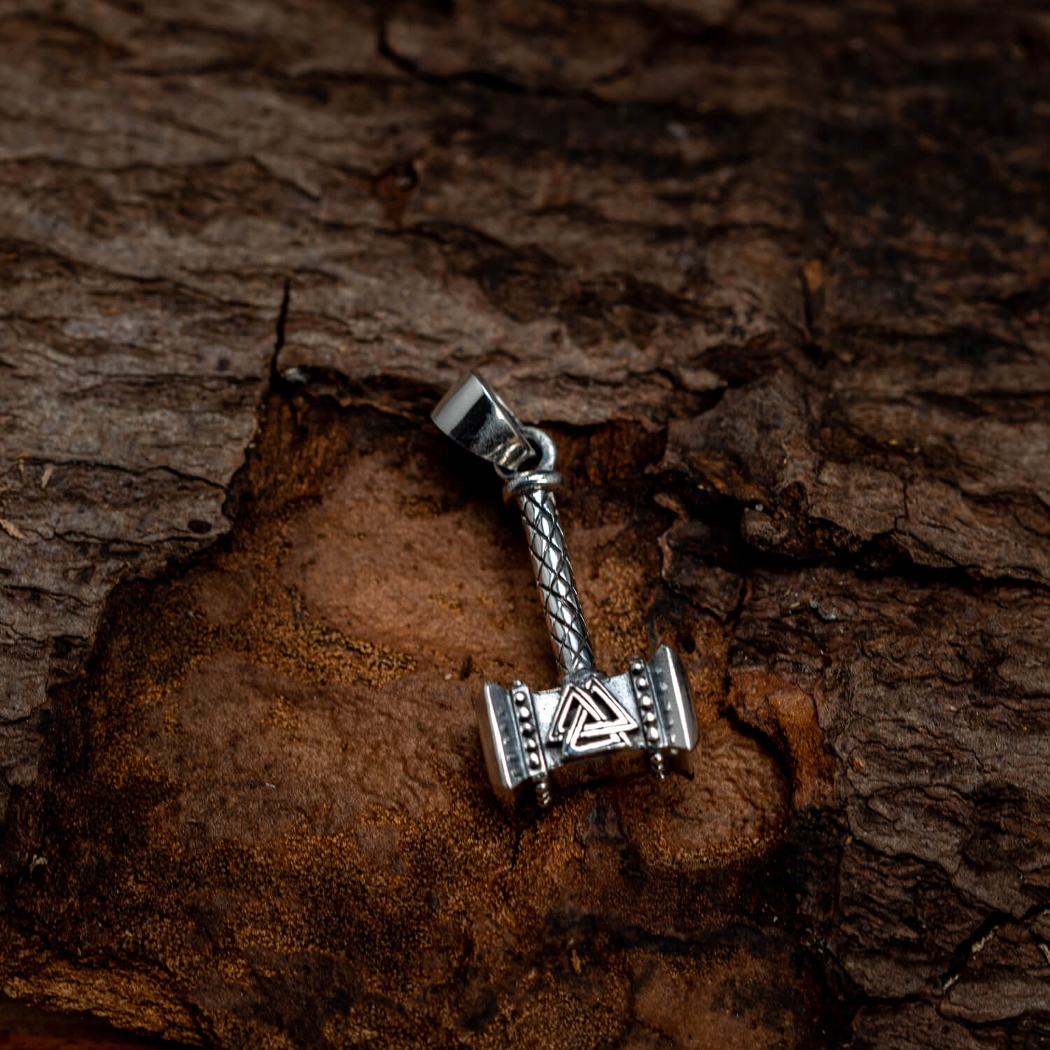 En detaljeret Thors Hammer Trial Vedhæng 925s Sterling Sølv, formet som Thors hammer (Mjölnir), med indviklede mønstre og et trekantet design i midten, er placeret mod en tekstureret træbaggrund. Vedhængets metalliske finish kontrasterer smukt med træets ruhed, og inkarnerer en simpel smykke-allure.