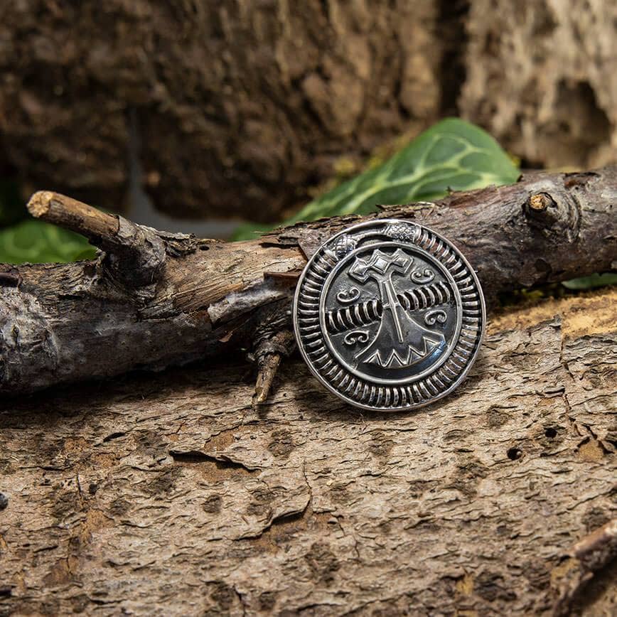 Et rundt, indviklet detaljeret stykke af Broche Vikingeskib Spænde 925s Sterling Sølv hviler mod den ru bark. Brochen har et symmetrisk design med et centralt vikingeskib, sandsynligvis af kulturel eller mytologisk betydning, omgivet af udsmykkede mønstre. Baggrunden inkluderer mere naturlige træteksturer og løv.