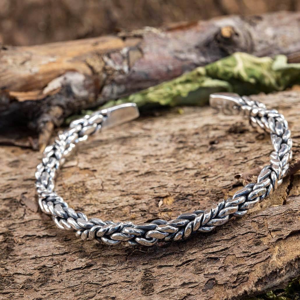 Armbånd Bangle Link 925s Sterling Sølv fremvises på en rustik træoverflade, der fremhæver dets indviklede, snoede design. Armbåndets detaljerede håndværk har sammenlåsende led, der skaber et smukt tekstureret mønster.