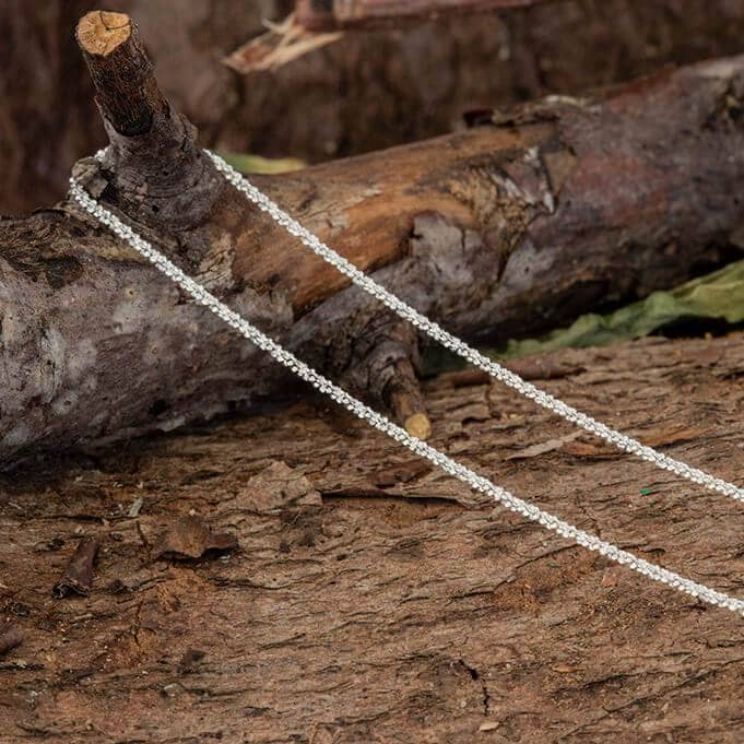 Halskæde Margherita 925s Sterling Sølv 1,5 mm med indviklede led er draperet over et stort stykke groft, tekstureret træ, der ligger på jorden omgivet af spredte blade. Kædens fine håndværk står i smuk kontrast til den robuste, naturlige baggrund.