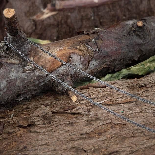 En delikat Halskæde Margherita Rhodineret 925s Sterling Sølv 1,5 mm halskæde er elegant draperet over et groft stykke naturligt træ, med en sløret baggrund med endnu et stykke træ og nogle blade. De udendørs omgivelser fremhæver billedets rustikke og jordagtige fornemmelse.