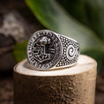 Bild in Galerie-Betrachter laden, En Sølvring Thors Hammer 925s Sølv-ring med et detaljeret design hviler på en stenoverflade. Ringens ansigt viser et indviklet mønster med runesymboler, der omkranser et centralt billede af den nordiske hammer, Mjolnir. Siderne har hvirvlende og prikkede designs, mens grønne blade sløres i baggrunden.
