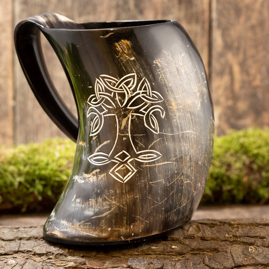 Et poleret, buet Vikingekrus Yggdrasil-horn (600-800 ml) med et håndtag, med en indviklet hvid indgravering af et symmetrisk, keltisk-inspireret design. Drikkehornskoppen er sat på en rustik træbaggrund med grønt mos og en forvitret træoverflade.