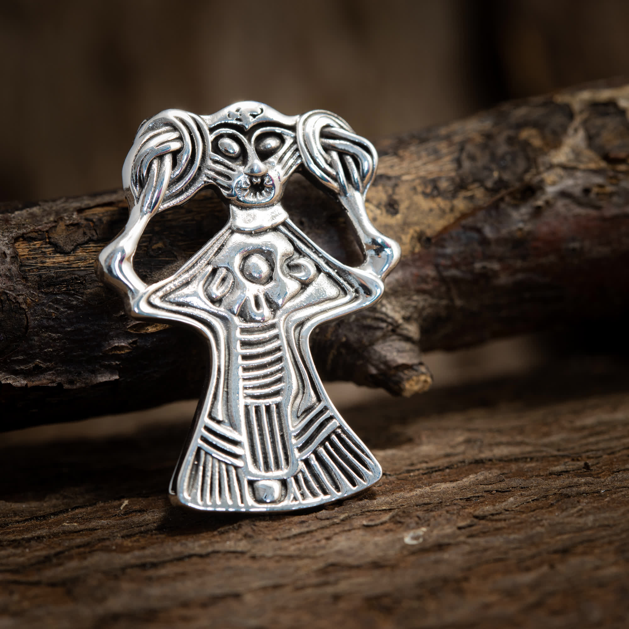 Et nærbillede af en Freja Amulet Vedhæng 925s Sterling Sølv designet i en abstrakt menneskelig form med detaljerede mønstre. Sterling Sølv smykke ligger på en rustik træbaggrund og viser sine indviklede udskæringer og kunstneriske håndværk.