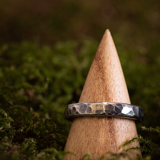 En indviklet Fingerring - Eryn Design - Guarding in 925s Sterling sølv hviler på en trækegle, omgivet af frodigt grønt mos. Ringens design viser subtile variationer i lys og skygge mod de naturlige omgivelser.