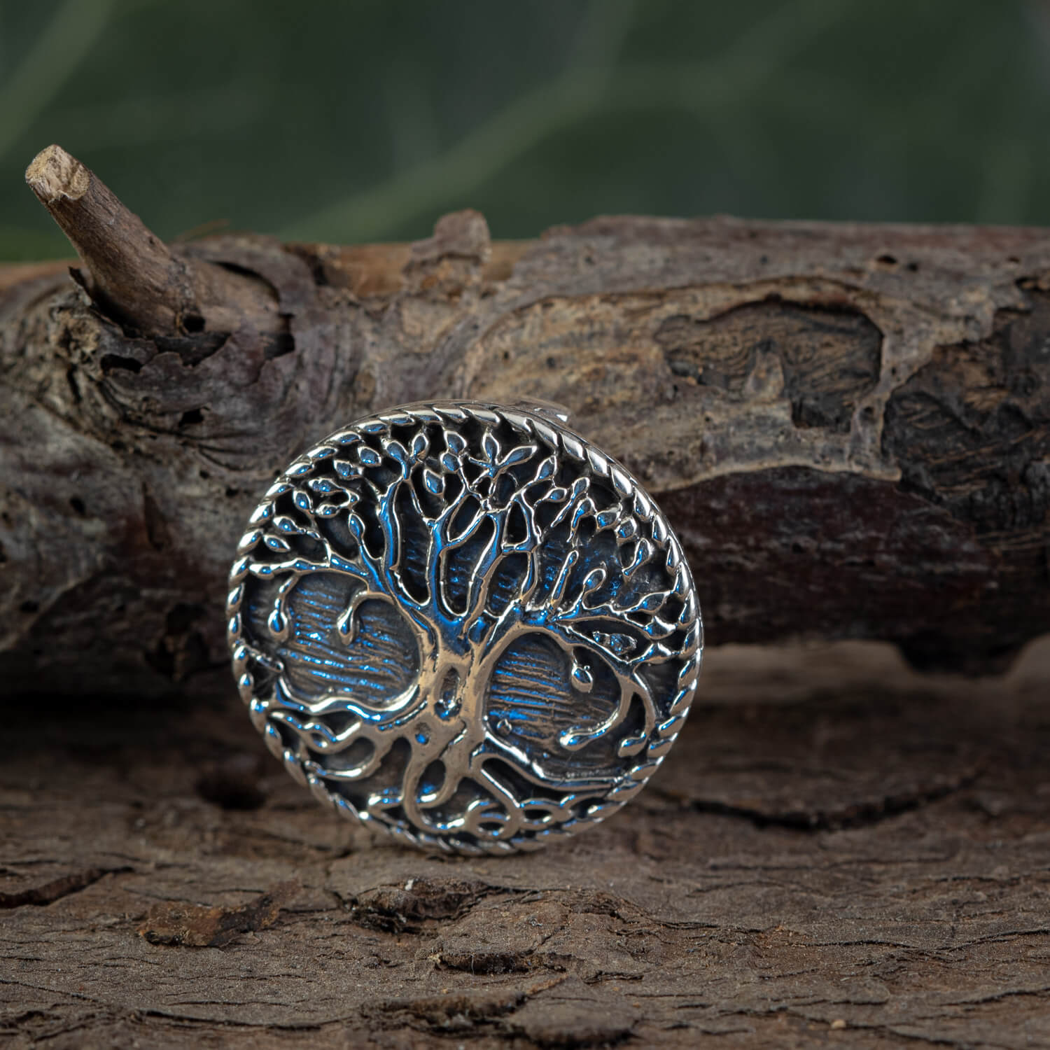 En amulet ved navn Yggdrasil Livets Træ Vedhæng, lavet af 925'erne Sterling Sølv, med et detaljeret trædesign med indviklede grene og rødder, er placeret på en ru træoverflade. Baggrunden er blødt sløret og fremhæver vikingesmykkens metalliske og polerede tekstur.